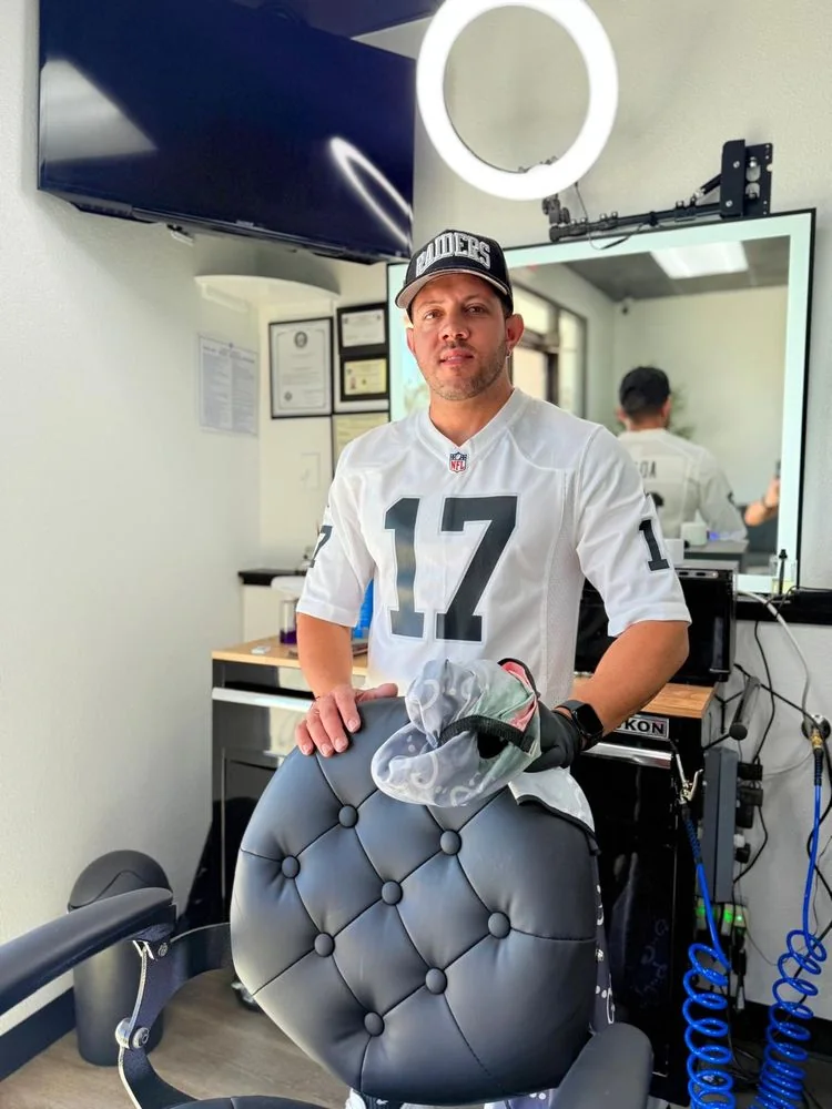 The owner of Duran's Barbershop standing at the barber chair inside the shop